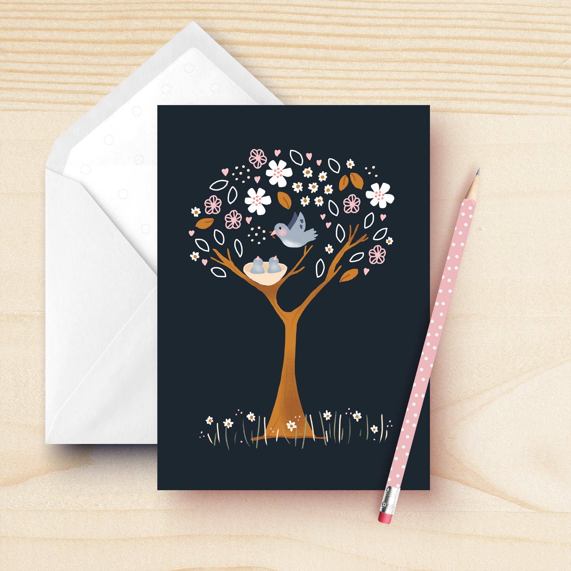Blank greeting card geaturing a blue bird feeding it's young babies in the nes. The tree is a beautiful pink and white floral tree on a dark blue background. Hand drawn by Kathrin Legg