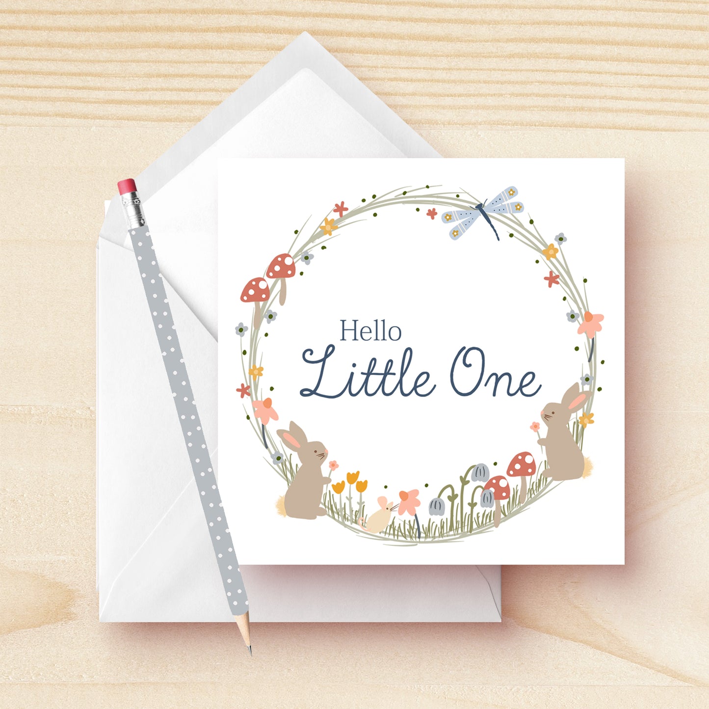 Hello Little One new baby greeting card hand drawn by Kathrin Legg. A beautiful, soft pastel woodland wreath illustratoin featuring small baby rabbits, mushrooms and a dragon fly with the words 'Hello Little One' featured in the centre of the wreath.